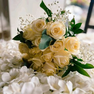 A bouquet of creamy white roses with green leaves on white petals.