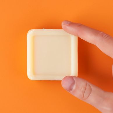 Two fingers touching a square light yellow bar soap.