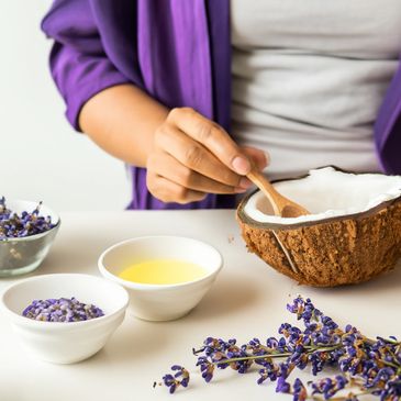 A lady stirring with a wood spoon inside half of a coconut. On the table 3 small containers.