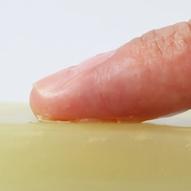 Close up to a finger (top) robing a bar soap  (bottom) seen from the side.