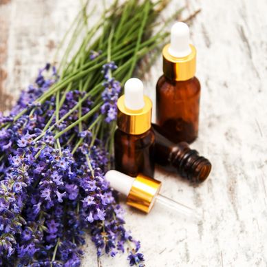 Lavender flowers on a table with 3 essential oil amber bottles: 2 closed and 1 opened.