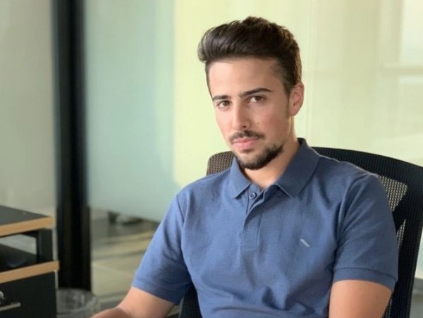 Young man in blue polo shirt sitting on office chair.