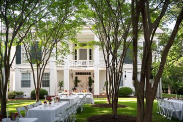 Outdoor dining setup in front of a large white house.