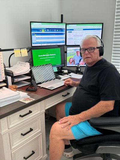 Older man working at a computer desk with multiple monitors.