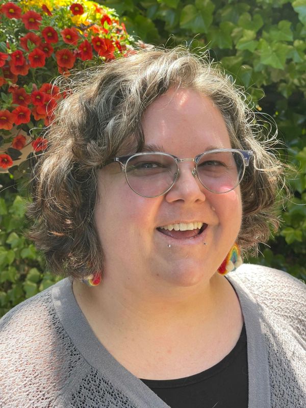 Smiling woman with glasses and curly hair outdoors.