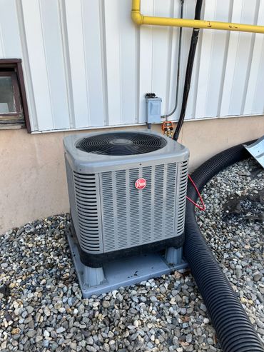 Rheem air conditioning unit installed outside on a bed of rocks.