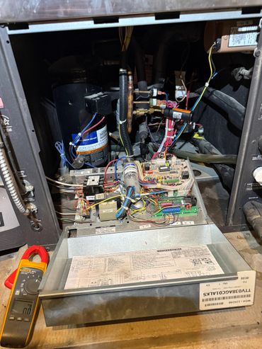 Open HVAC unit showing internal wiring and components with a clamp meter nearby.