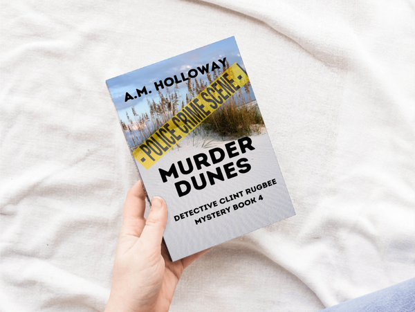 Person holding a mystery book titled Murder Dunes by A.M. Holloway.