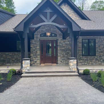 Modern house entrance with stone pillars and wooden door.