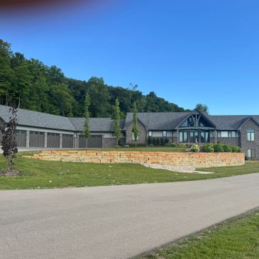 Modern house with stone retaining wall and lush greenery under a clear blue sky.