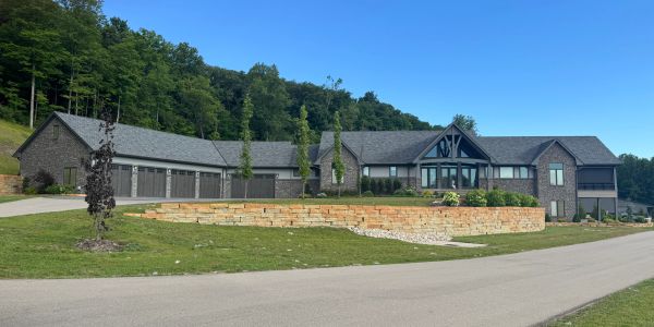 Large modern house with stone exterior and multiple garages under clear blue sky.
