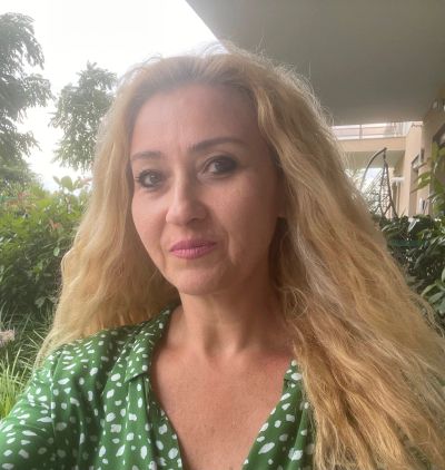 Woman with long blonde hair in green polka dot blouse outside.
