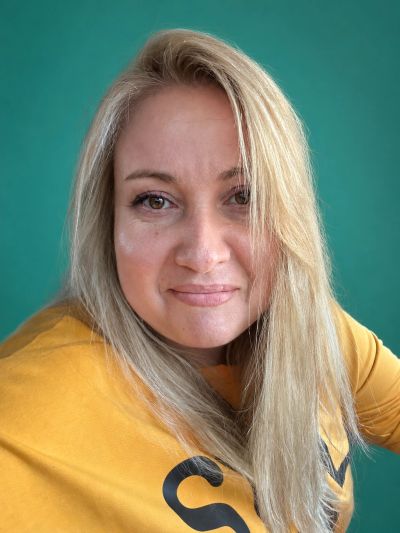 Blonde woman smiling in a mustard yellow top.