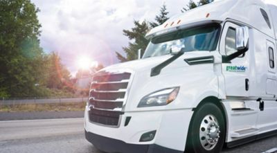 White semi-truck with 'greatwide' logo on a highway during sunset.