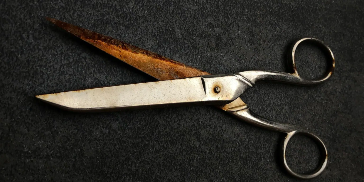 Old rusty scissors on black surface.