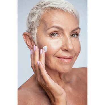 Smiling mature woman applying face cream for skincare.
