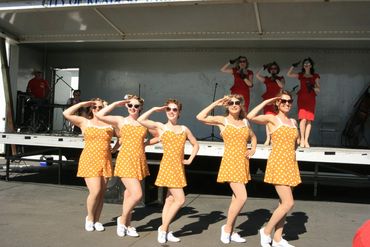 Women dressed up in era inspired dressed (both red and yellow) saluting.
