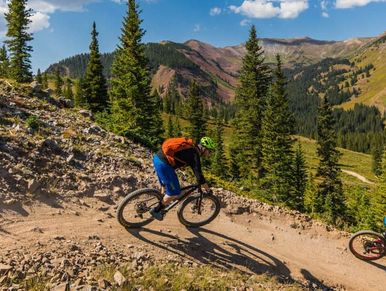 Man riding bike on dirt path over looking trees and a mountain.