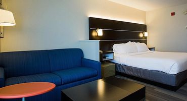Suite with a bed with white bedding, a blue couch, and orange coffee table.