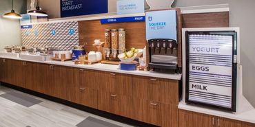 Breakfast area with juices, pastries, coffee, and a fridge with yogurt, fruit, eggs, and milk.