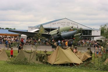WWII military tents and aircrafts surrounded by weekend crowd.