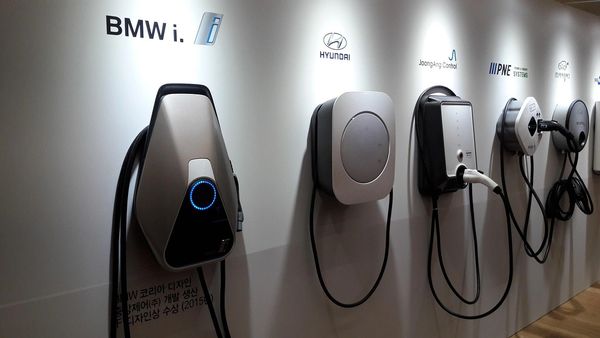 Row of electric vehicle charging stations from various brands mounted on a wall.