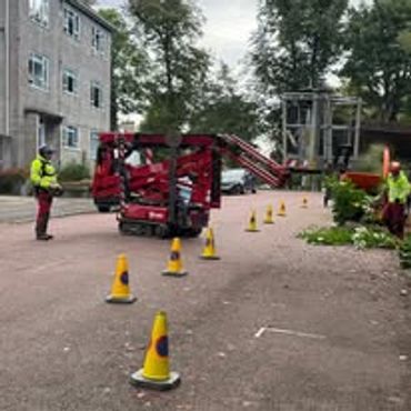 Construction workers operating red machinery near a building.
