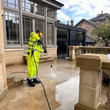 Worker cleaning stone pavement with pressure washer.
