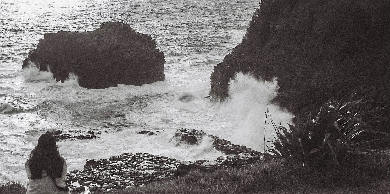 Person looking at waves crashing on rocky shore.