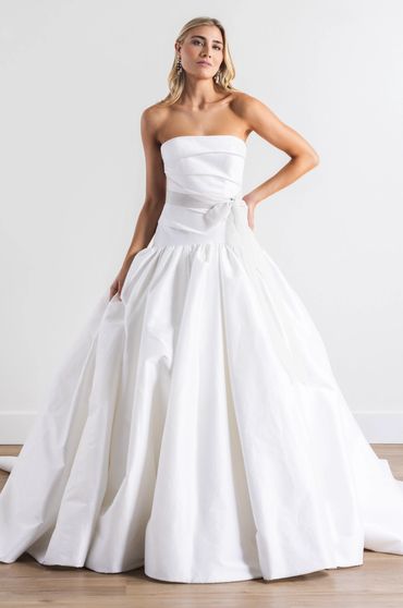 A classic drop waist wedding gown with a ruched bodice and pleated skirt featuring a delicate bow