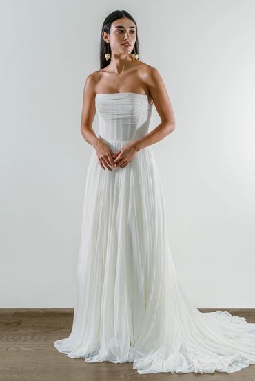 An A-line organic style wedding dress with a straight neckline and pleated skirt featuring exposed b