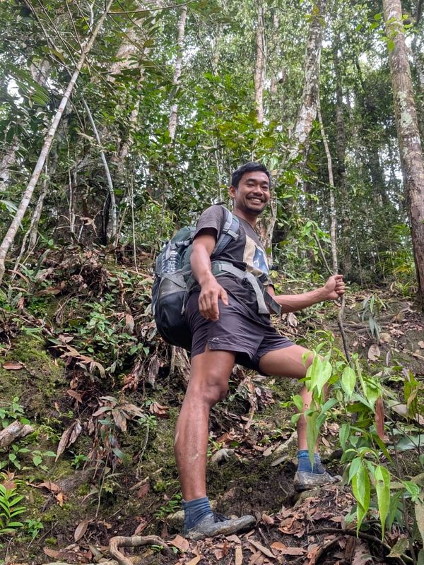 Andri, a smiling local jungle guide trekking in the rainforest of Bukit Lawang, Sumatra.