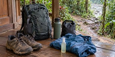 Trekking shoes, backpack, rain jacket, water bottle and dry bag for a rainforest trek.