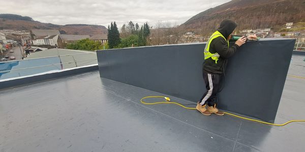 Worker in safety vest working on rooftop edge with tool.