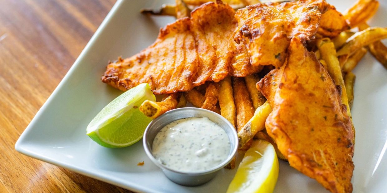 A plate of fish and chips with a dip on a white color plate
