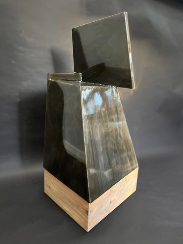 Abstract geometric sculpture with glossy black and natural wood base.