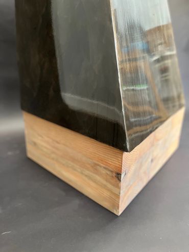 Close-up of metal sculpture with a wooden base on a dark surface.