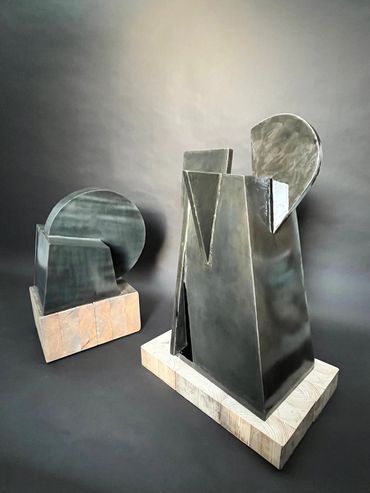 Abstract metal sculptures on wooden bases against a dark background.