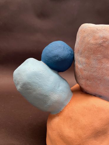 Balancing Rocks Abstract sculpture with blue, light blue, and terracotta shapes against brown.