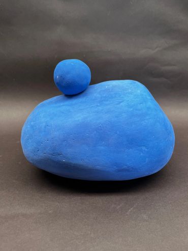 Two blue clay shapes, one round and one oval, against a dark background.