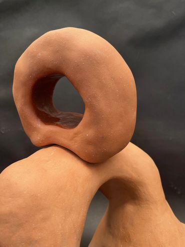 Abstract terracotta sculpture with smooth, curved shapes against a dark background.