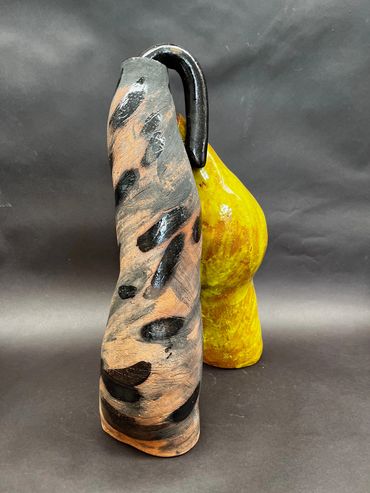 Abstract ceramic sculpture with black and yellow shapes on a dark background.