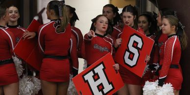 Cheerleaders holding signs and pom-poms, dressed in red uniforms.