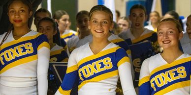 Cheerleaders in blue and yellow FOXES uniforms smiling confidently.