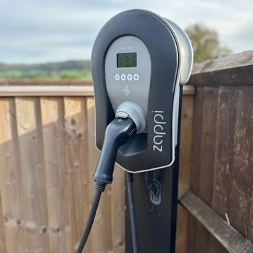 Electric vehicle charging station with a plugged-in charger outdoors.