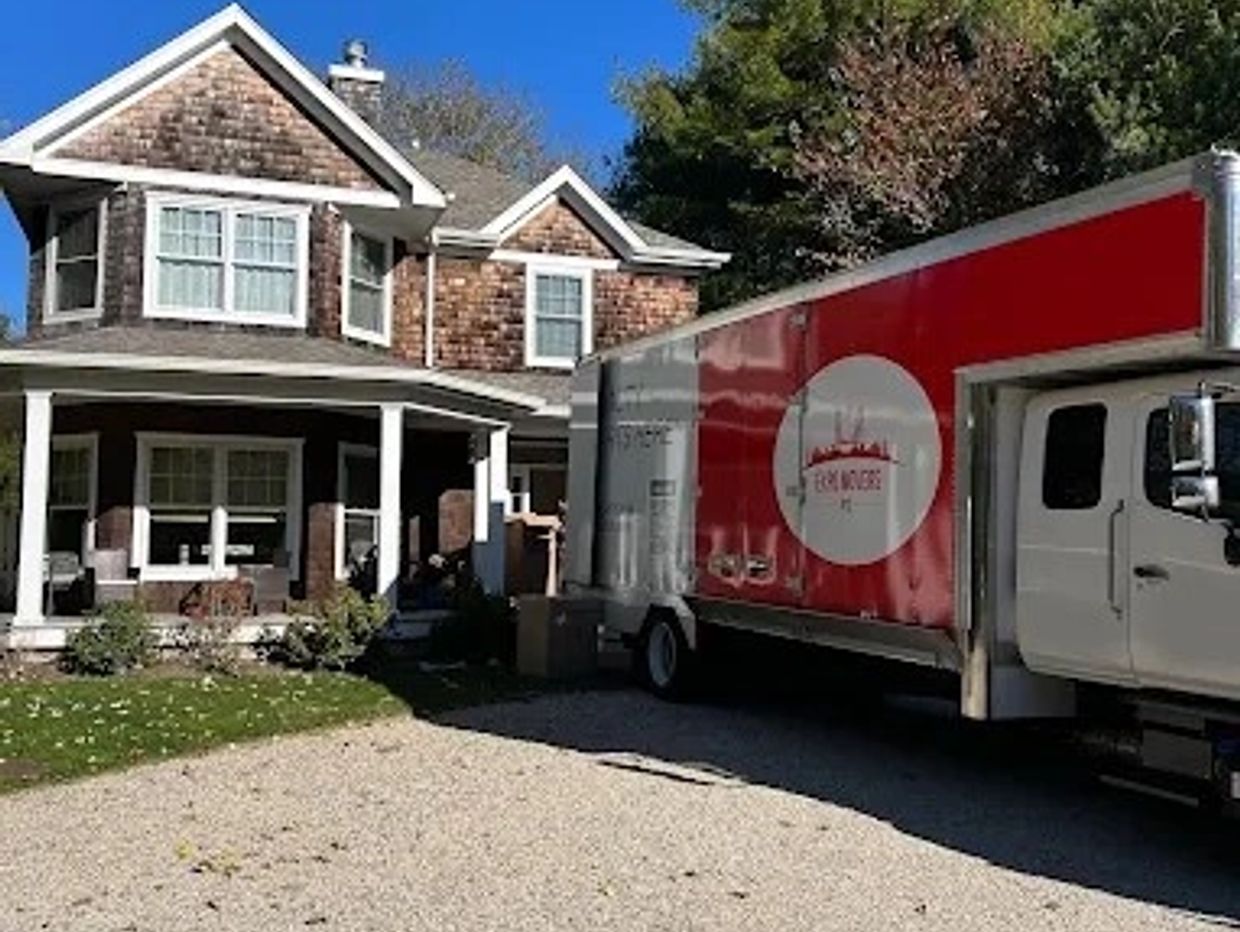 Moving truck parked outside a large suburban house on a sunny day.