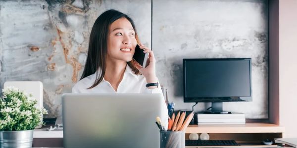 A woman talking on the phone in front of a laptop screen