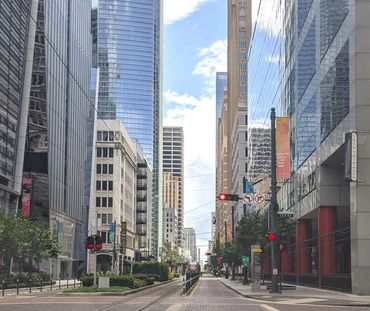Empty city street lined with tall buildings and red traffic lights.