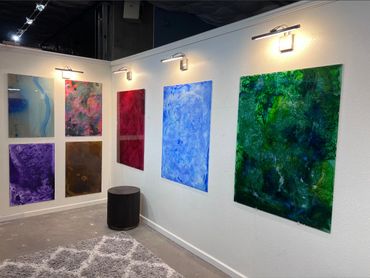 Colorful abstract paintings displayed on a white gallery wall with lighting.
