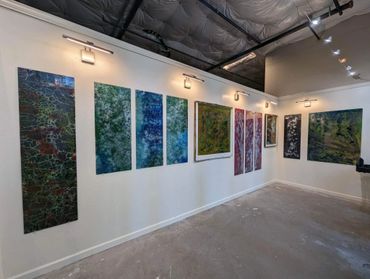 Abstract paintings displayed on a white gallery wall under spotlighting.